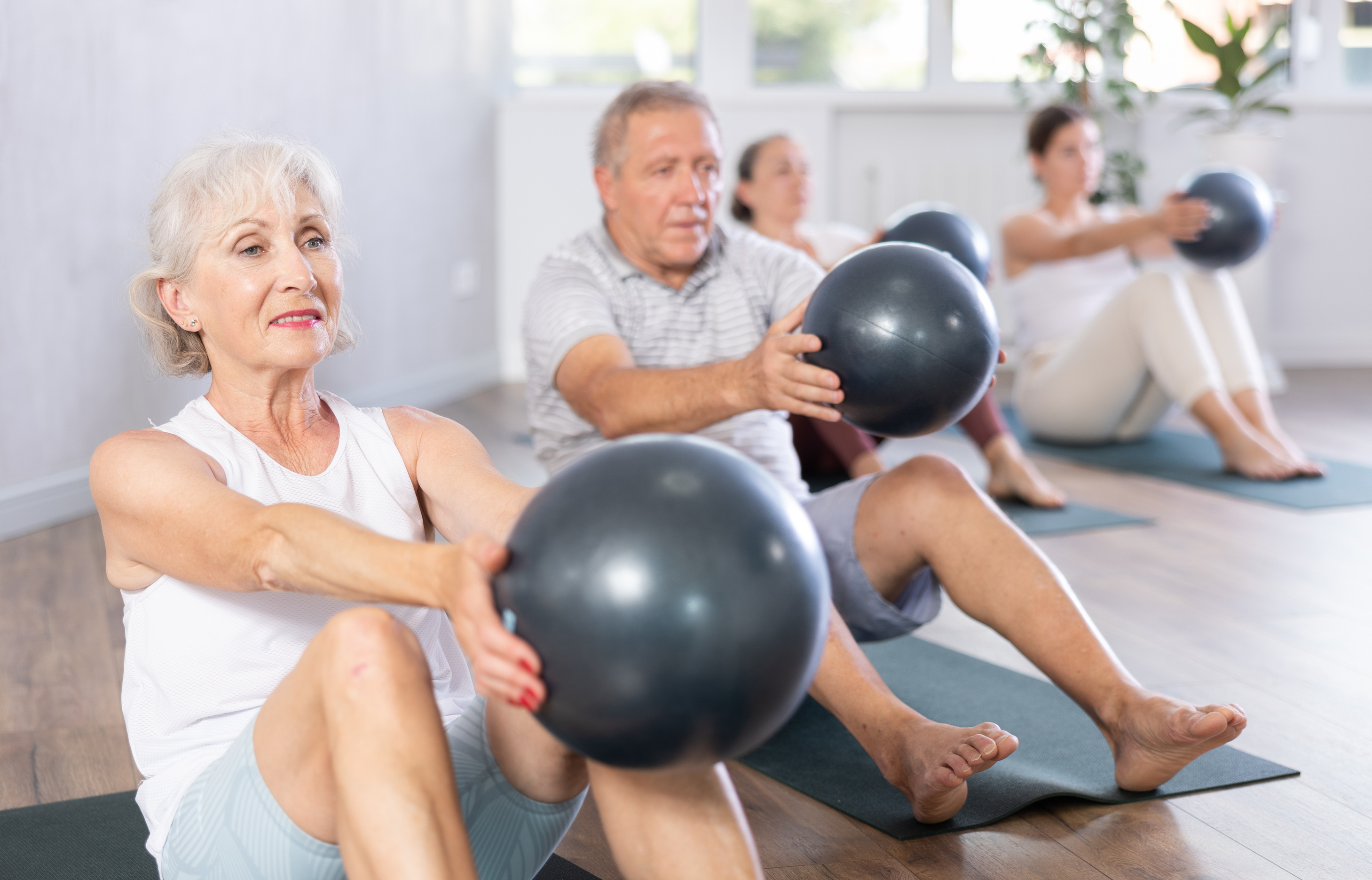 Portrait of elderly people doing exercises for press with pilates ball during group class in fitness studio