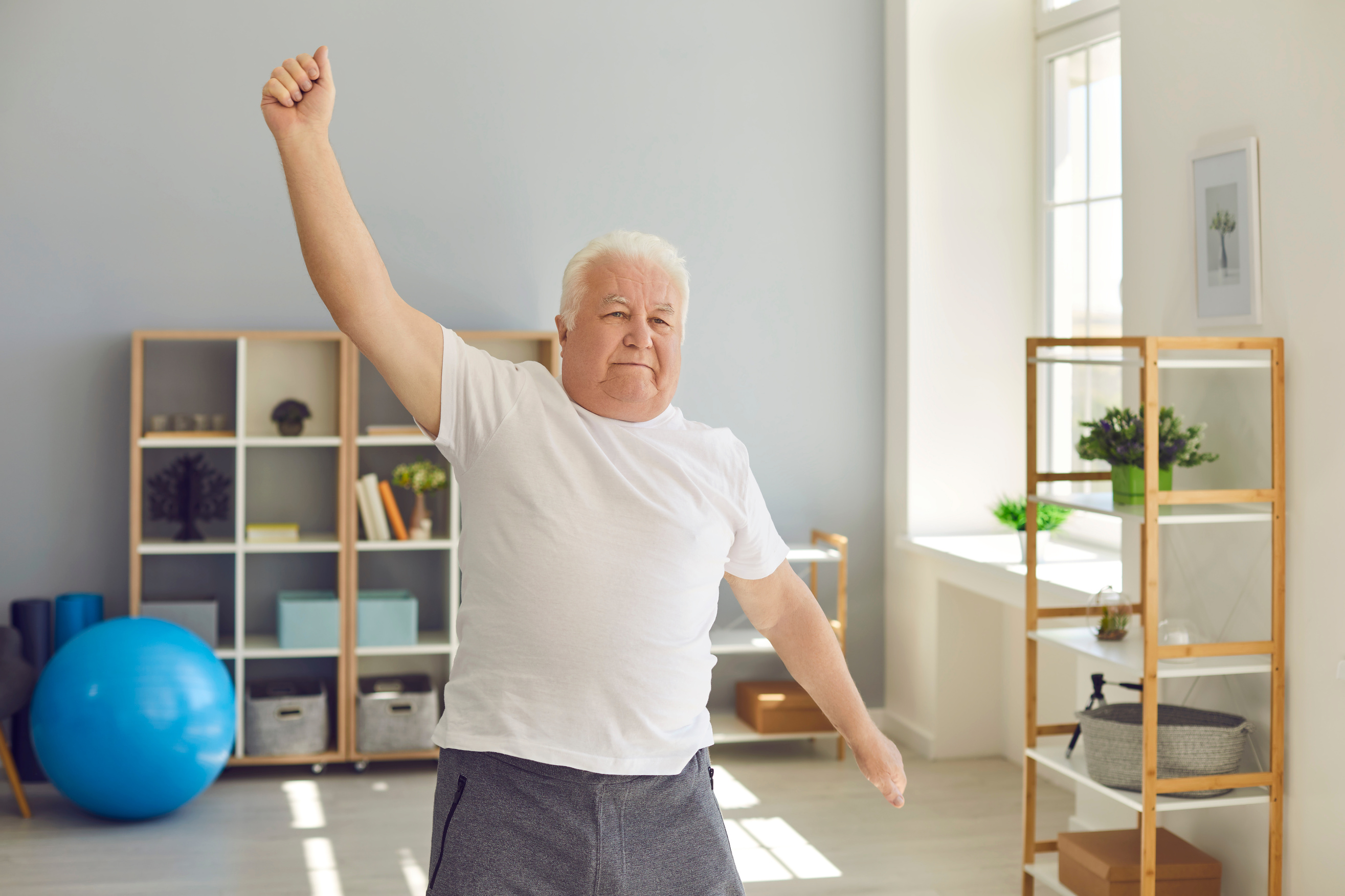 Smiling Positive Elderly Man Doing Exercises or Light Fitness Training at Home or in Rehabilitation Center